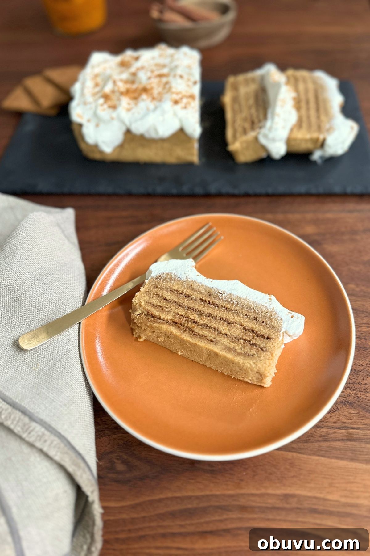 No-Bake Pumpkin Icebox Cake for Fall Desserts 9 A slice of pumpkin icebox cake topped with whipped cream on an orange plate, ready to eat.