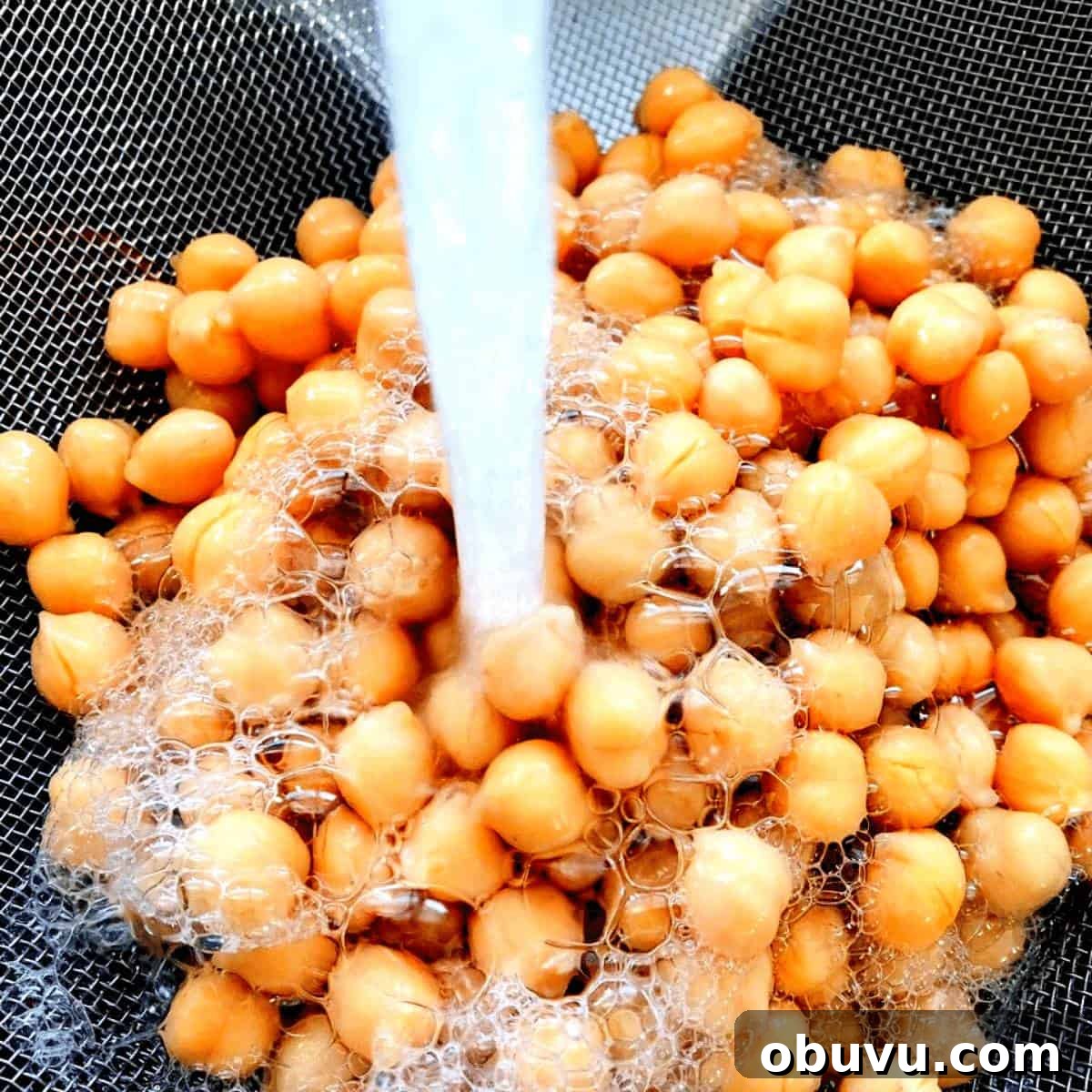A can of chickpeas in a strainer being rinsed with water.