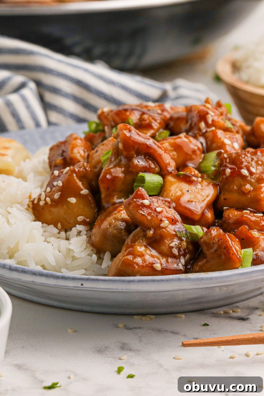 30-Minute Bourbon Chicken Skillet Recipe That Beats Takeout 11 plate with some diced bourbon chicken ad a side of rice to side with a striped grey towel behind it on the table