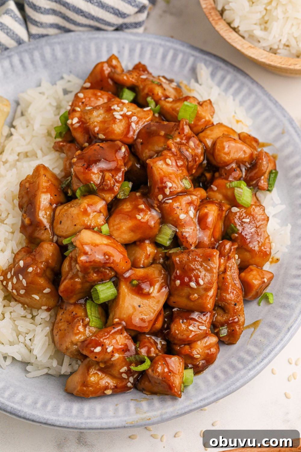 30-Minute Bourbon Chicken Skillet Recipe That Beats Takeout 12 looking down on table with a plate full of diced skillet bourbon chicken and a bed of rice to the side and a red and grey striped towel to side
