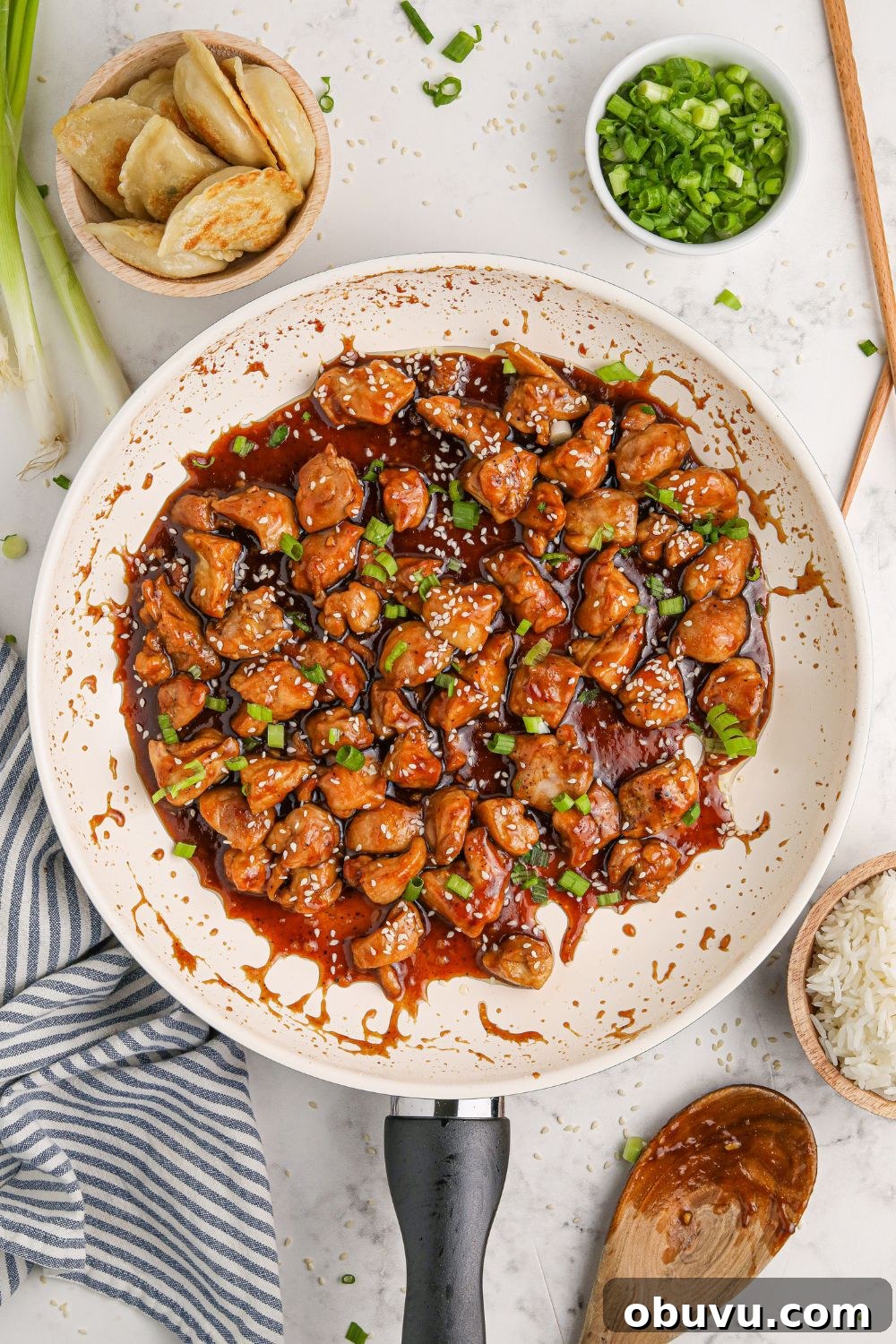 30-Minute Bourbon Chicken Skillet Recipe That Beats Takeout 13 a skillet on the table with diced Bourbon Chicken Skillet to the side and green onions to the side on the plate