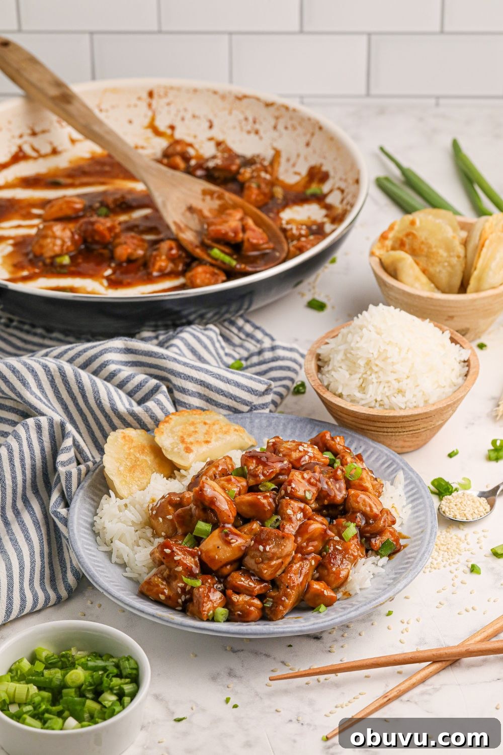 30-Minute Bourbon Chicken Skillet Recipe That Beats Takeout 14 Bourbon Chicken in a skillet with a plate full of chicken and rice in front, a bowl of rice, and pieorgi's as well all on a dinner table