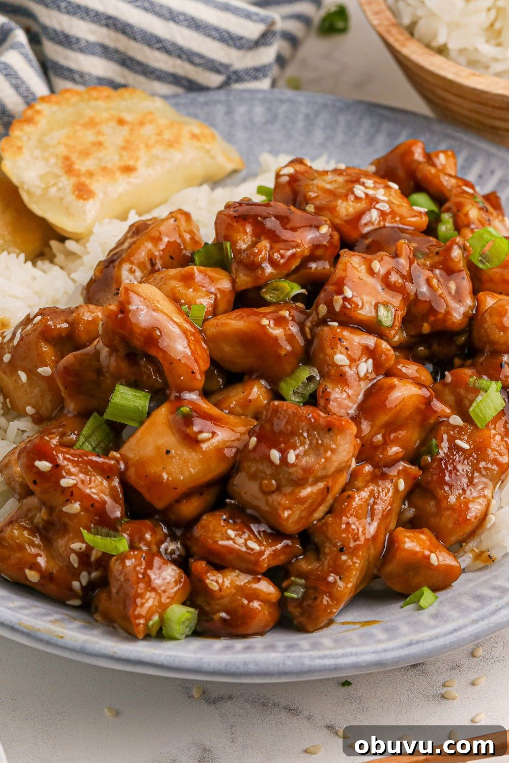 30-Minute Bourbon Chicken Skillet Recipe That Beats Takeout 15 close up look of all the bourbon chicken on a blue plate on the table with some rice to the side of the plate and a bowl of more rice behind the plate