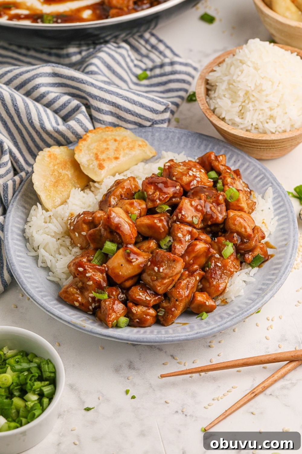 30-Minute Bourbon Chicken Skillet Recipe That Beats Takeout 17 a table full of bourbon chicken on plates, in a skillet, a bowl of green onions to the side, white rice in a bowl, and more