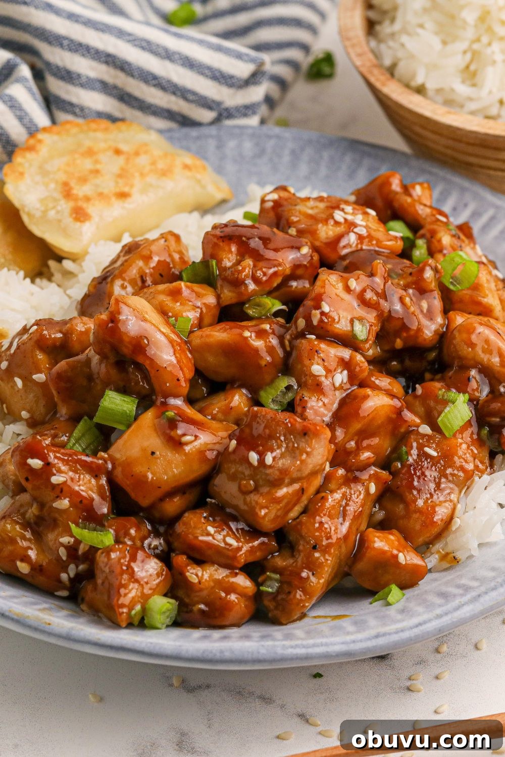 30-Minute Bourbon Chicken Skillet Recipe That Beats Takeout 19 a blue and white plate on table with diced bourbon chicken and white and pieorgies to the side on the the