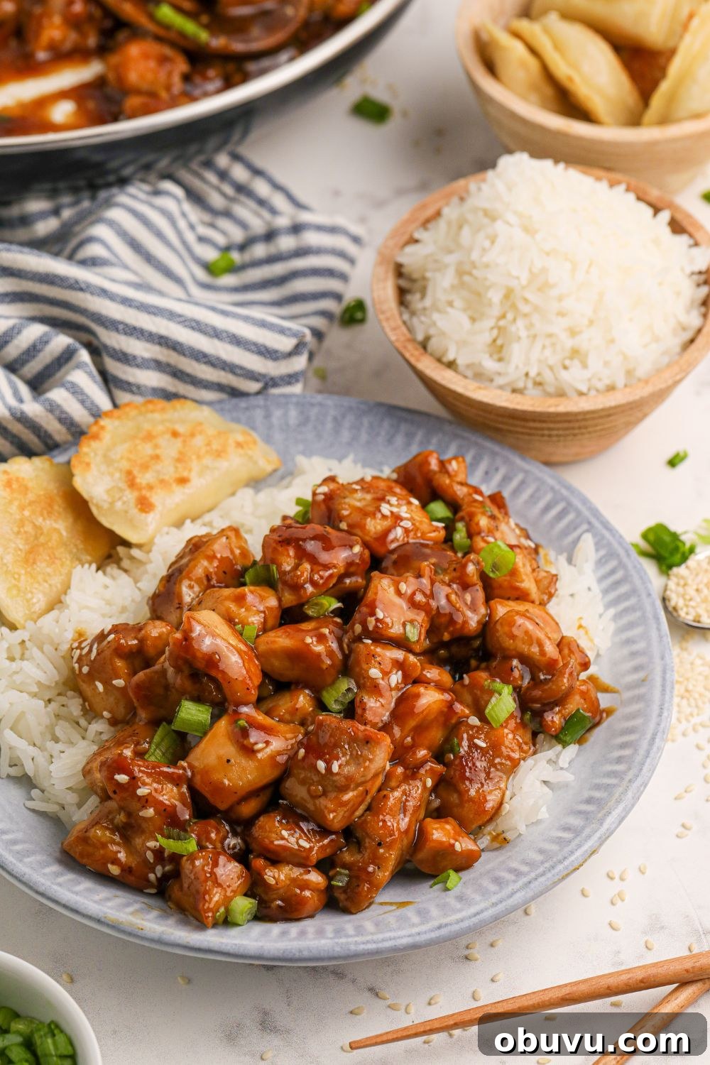 30-Minute Bourbon Chicken Skillet Recipe That Beats Takeout 4 Bourbon Chicken on a plate with rice to side and bread, with a bowl of rice and more chicken spread out on the table