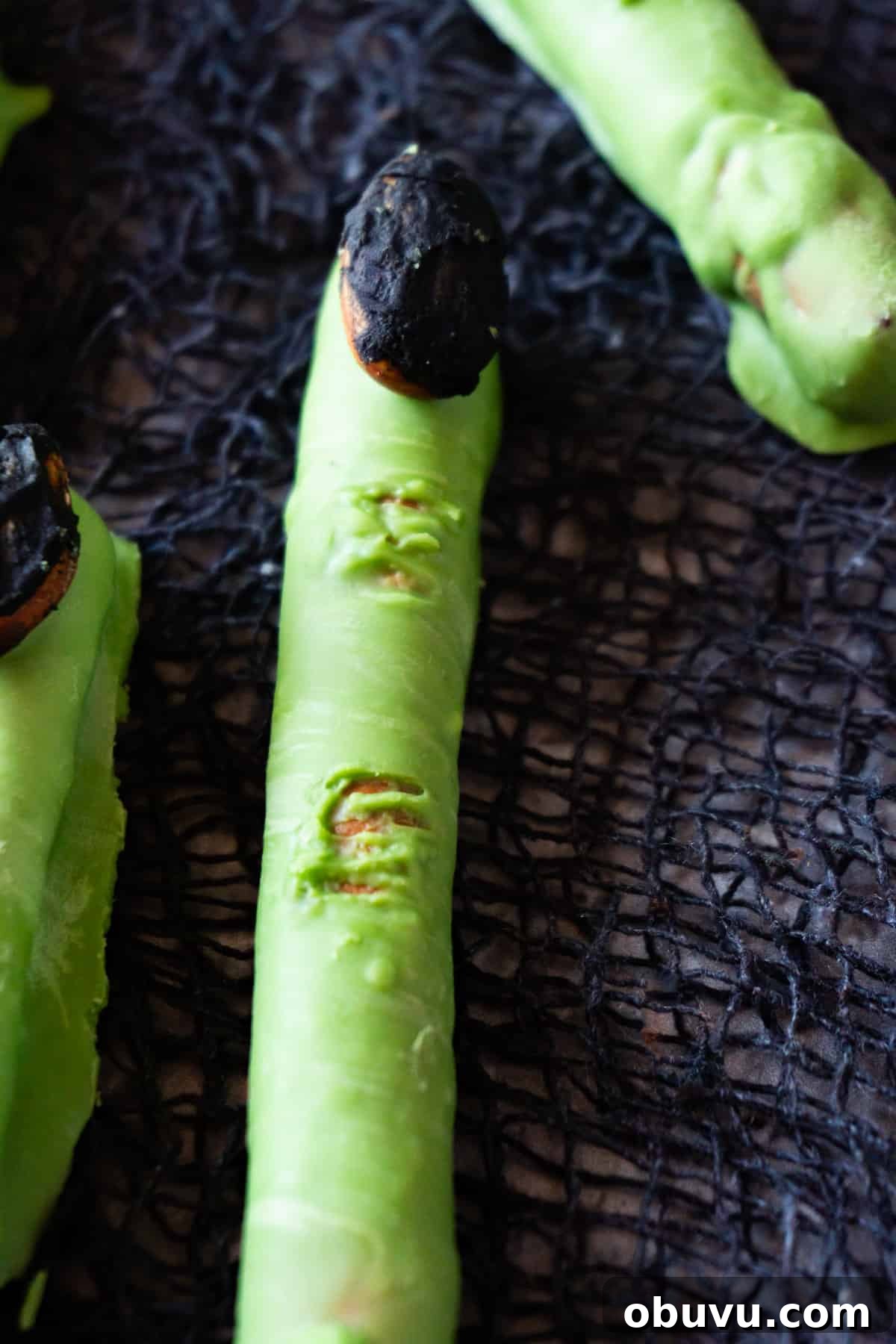 Witch Finger Cookies Recipe: Spooky Halloween Treats 3 green witch finger with black almond nail on mesh black background.