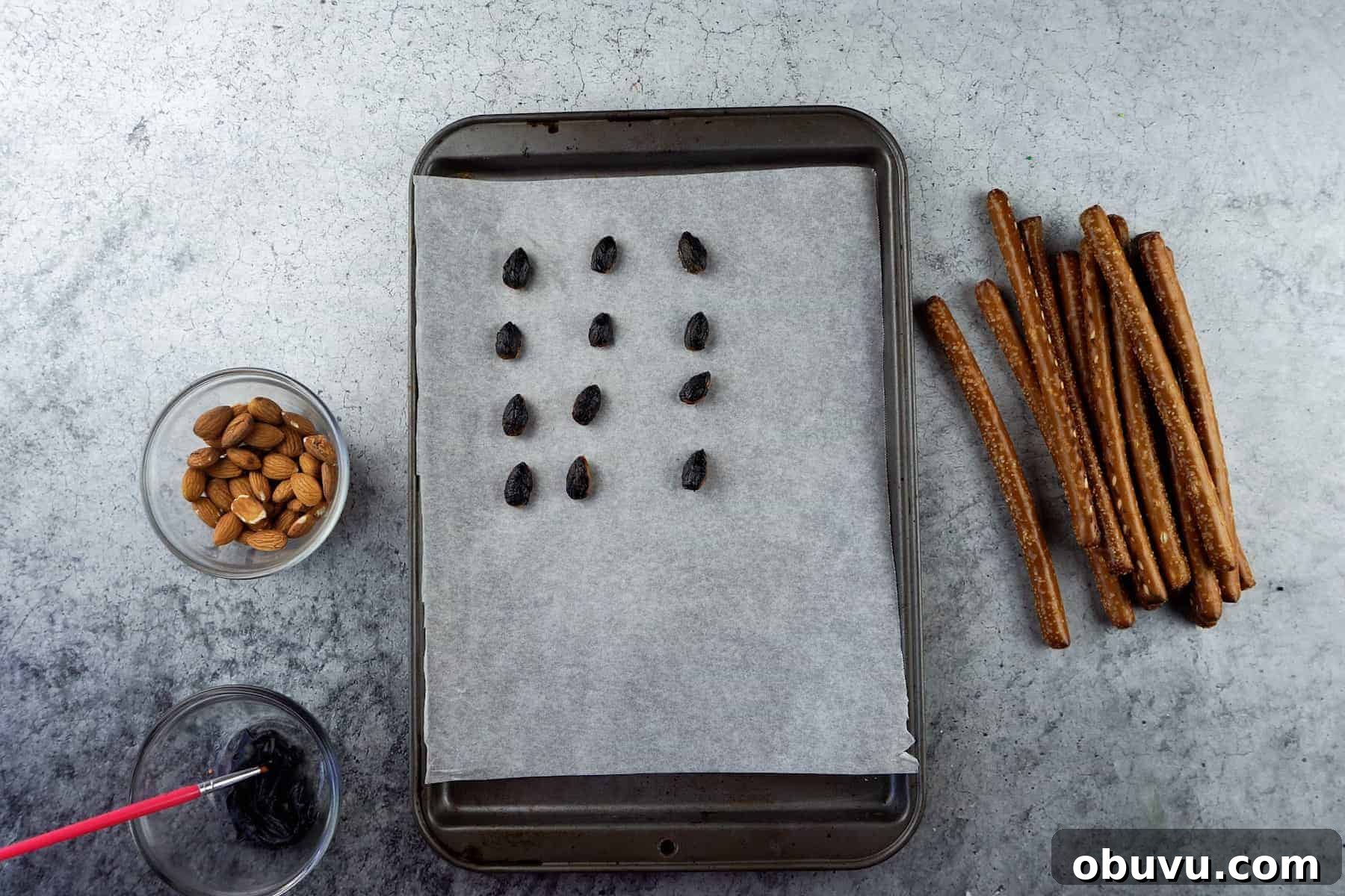 Witch Finger Cookies Recipe: Spooky Halloween Treats 5 almonds painted with black frosting on parchment-lined baking sheet.