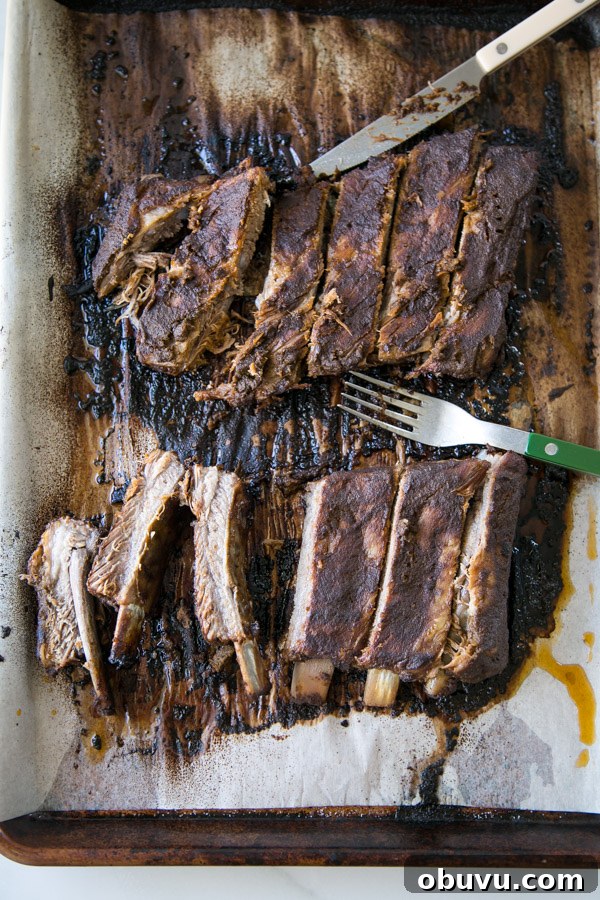Slow-Roasted Baby Back Ribs in 2½ Hours: Tender, Fall-Off-Bone 8 Sliced Oven baked Baby Back Ribs on a sheet pan with fork