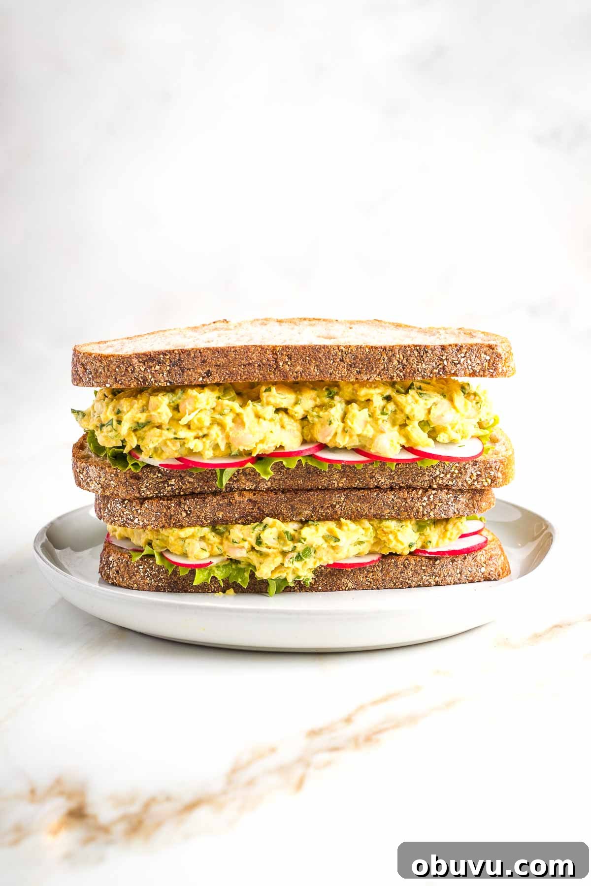 Crispy Vegan Chicken Salad with Creamy Herb Dressing 2 Stacked sandwiches filled with vegan curried chicken salad, lettuce and red radish slices.
