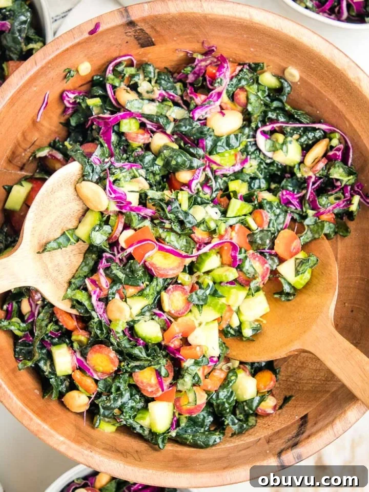 wooden salad bowl filled with colorful chopped salad: tuscan kale, purple carrots, red peppers, purple cabbage, cucumbers and marcona almonds