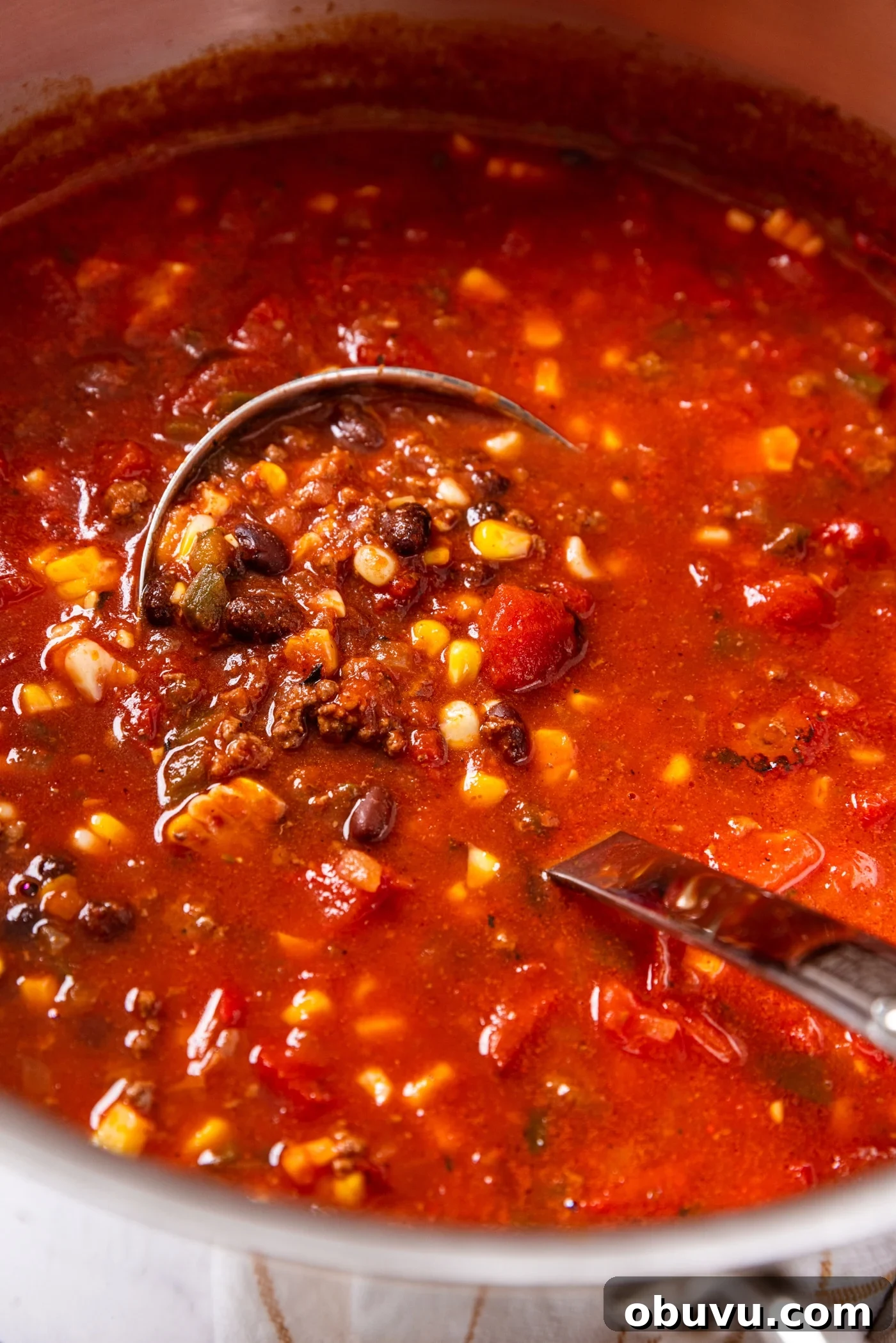 Quick Homemade Taco Soup Recipe for Cozy Weeknight Dinners 5 Metal stockpot filled with red-colored taco soup with pieces of corn, black beans, and browned beef showing as portion is held in metal ladle.
