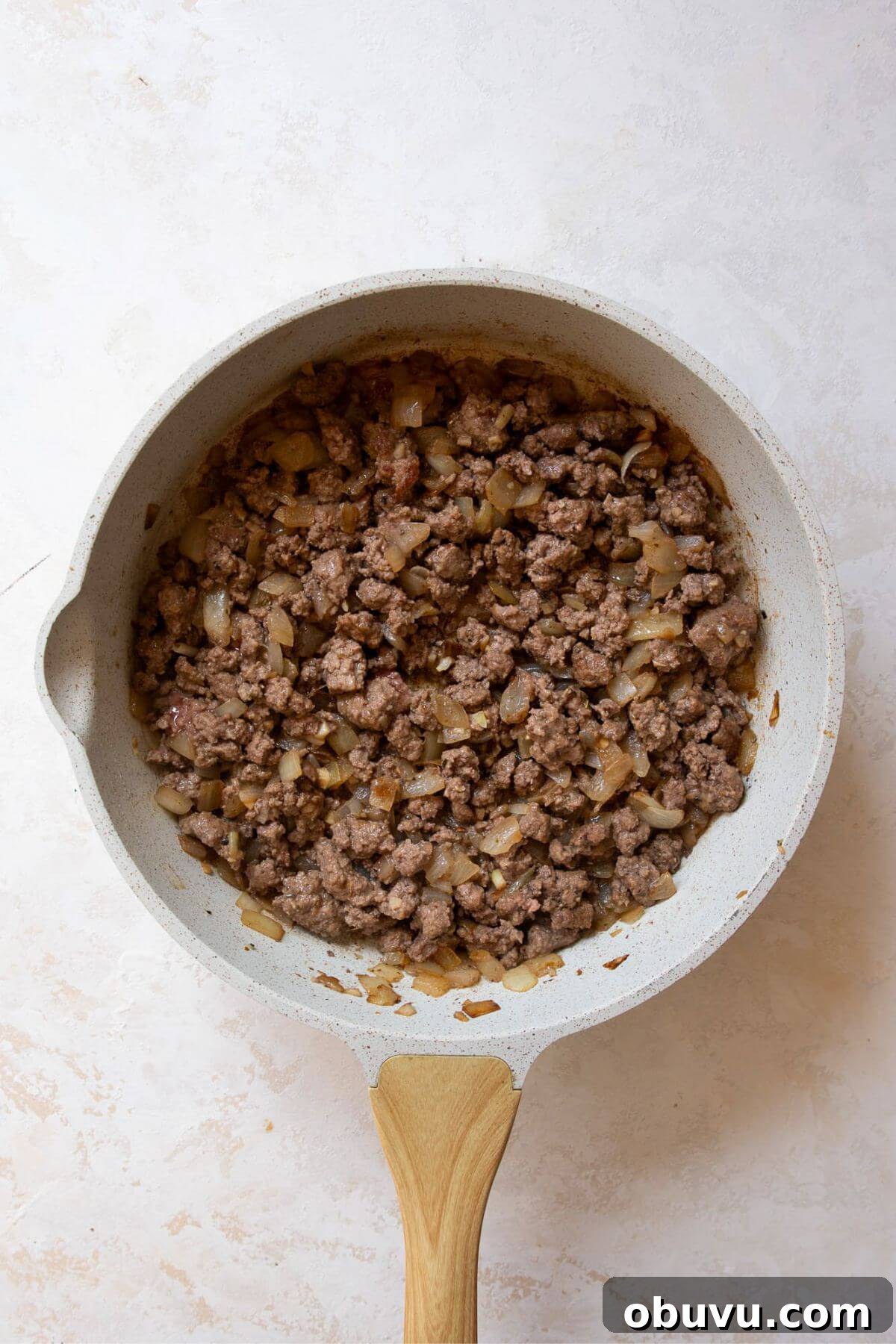 Ground beef browning in a skillet with sautéed onions and garlic.