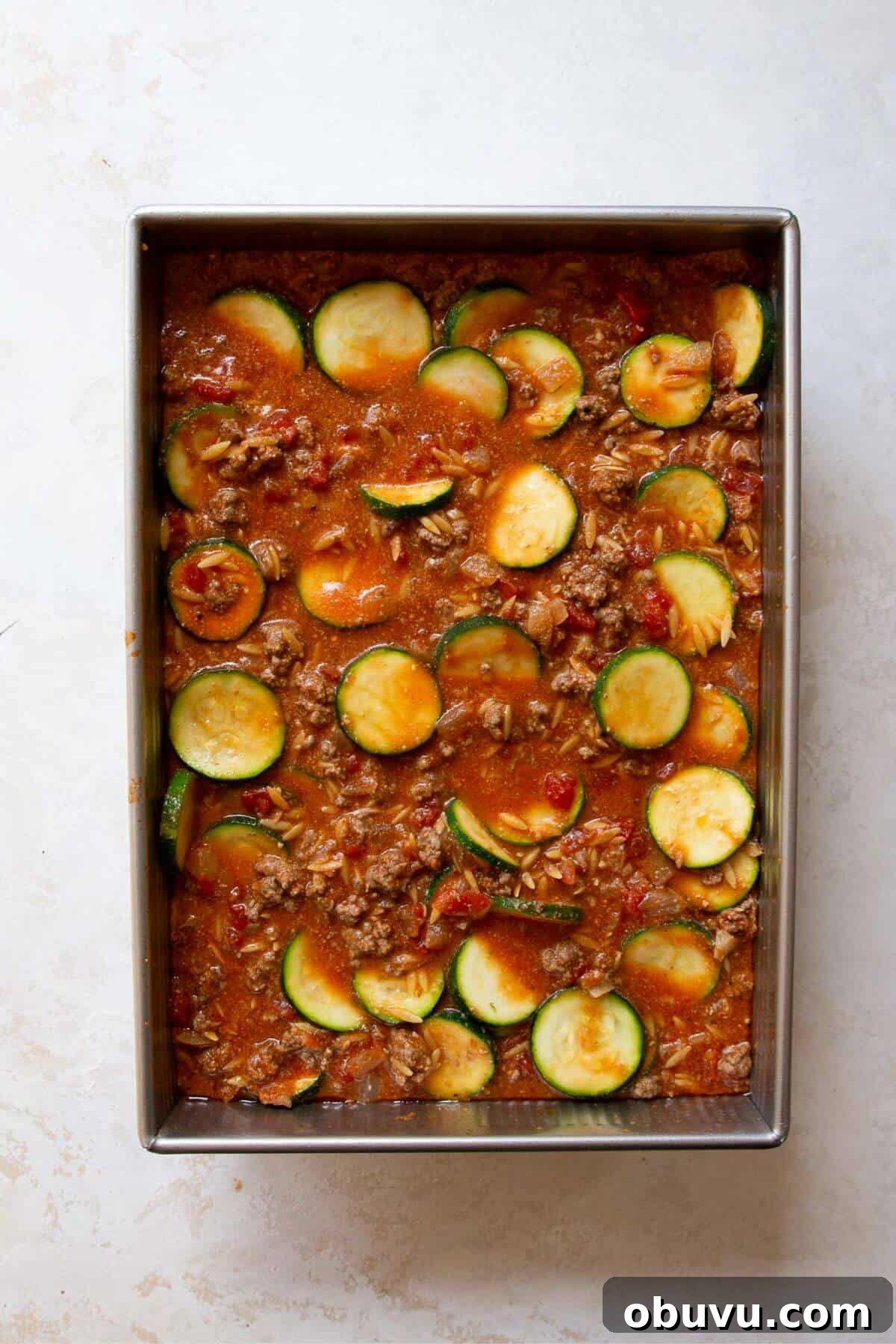 Casserole dish filled with ground beef sauce mixed with half the zucchini rounds, ready for layering before baking.