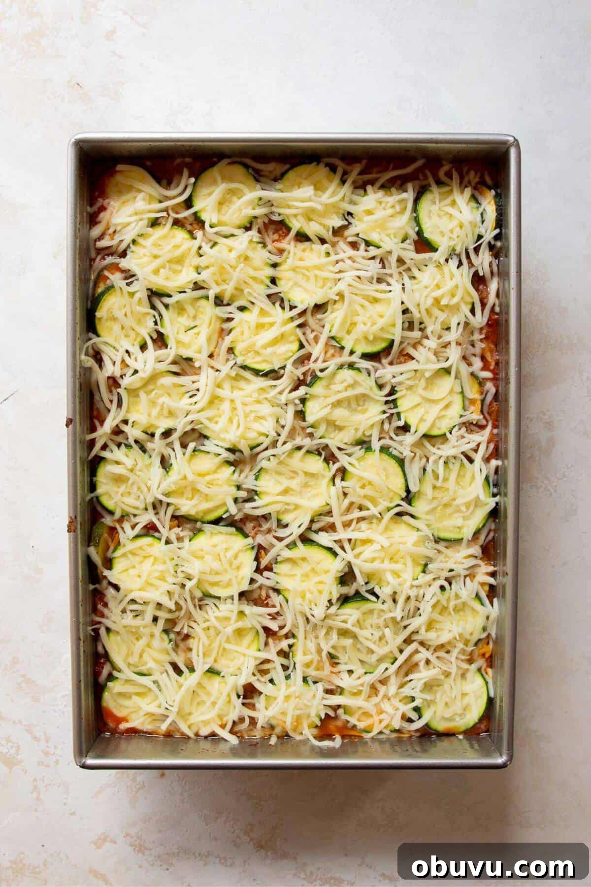 Adding a top layer of zucchini rounds and sprinkling mozzarella cheese over the ground beef casserole before baking.