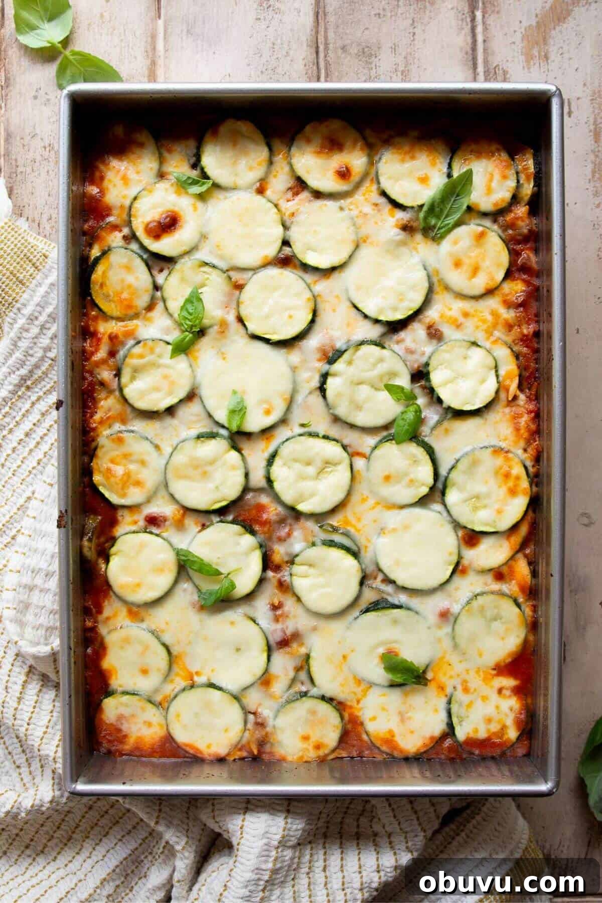 High-protein ground beef and zucchini casserole topped with melted cheese and fresh basil.