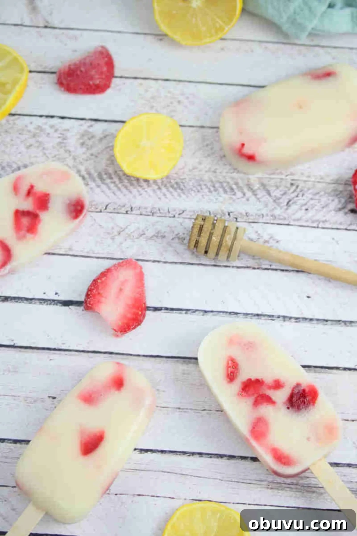 Strawberry yogurt protein popsicles laying flat with strawberries, a honey stick, and lemons around them.