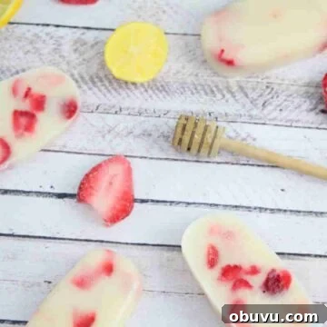 Strawberry yogurt protein popsicles laying flat with strawberries, a honey stick, and lemons around them.