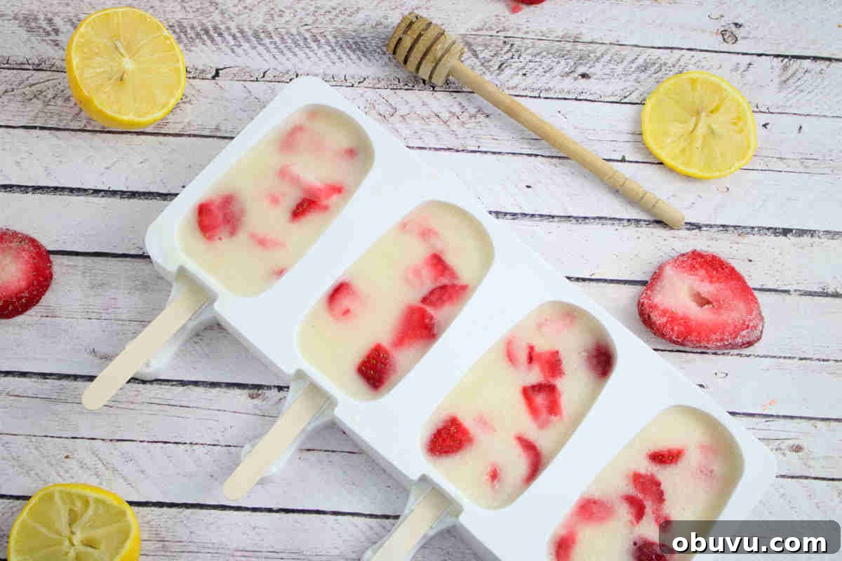 Protein popsicles with strawberries in a white silicone mold with berries, lemon, and honey around them.