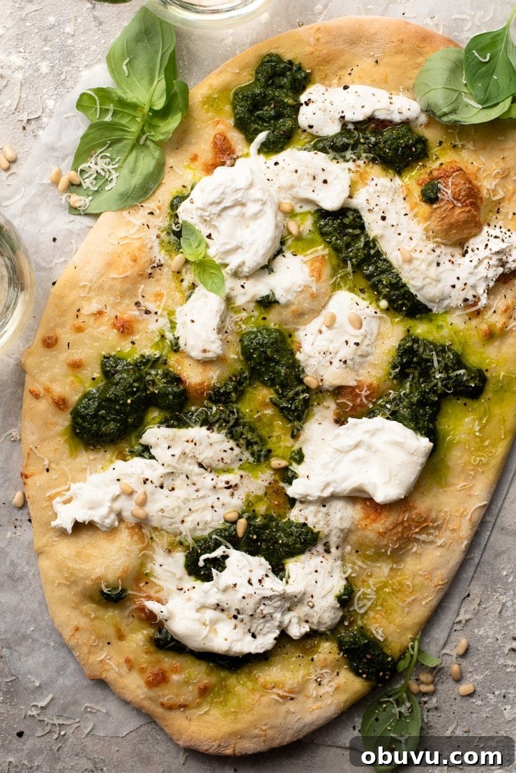 Homemade Cheesy Basil Pizza with fresh pesto, creamy burrata and pine nuts An overhead shot of a cheesy basil pizza with pesto and burrata