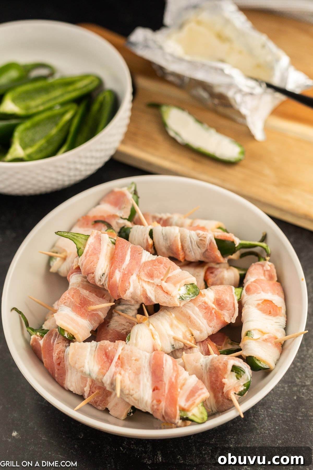 Smoky Grilled Jalapeño Poppers with Cream Cheese Filling 6 Wrapping the bacon around the jalapenos stuffed with cream cheese stacked in a bowl