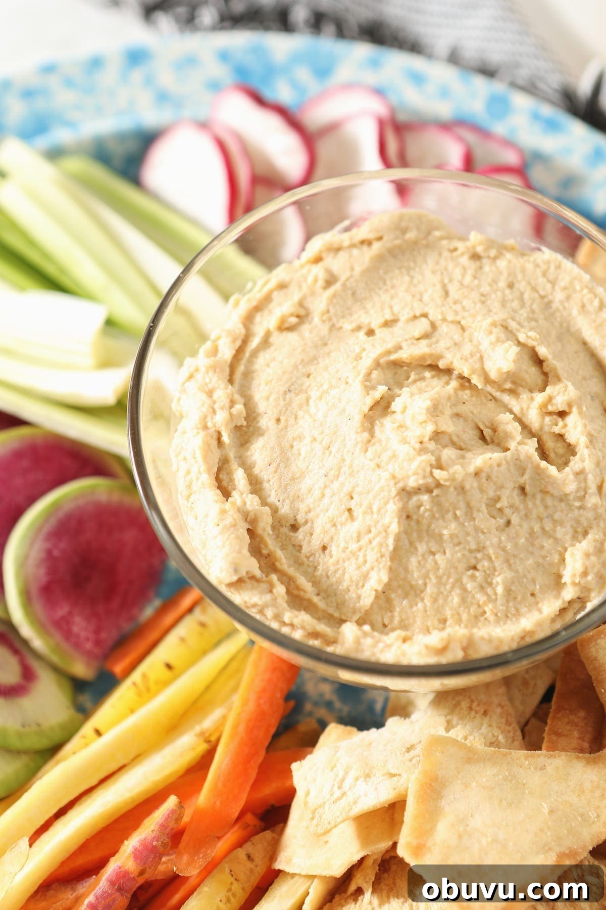 Winston’s Roasted Garlic Hummus Recipe 6 Close up of hummus dip in a clear glass bowl surrounded by veggie slices