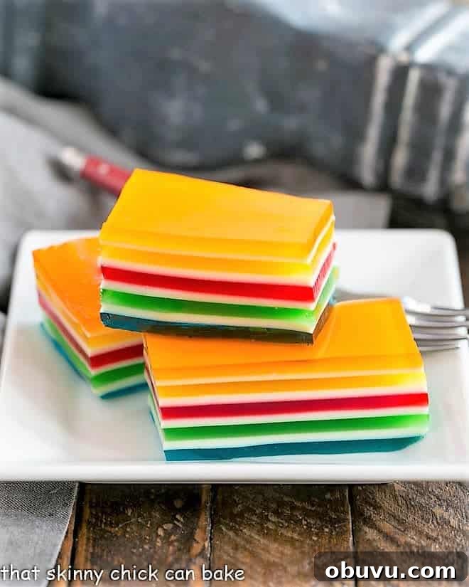 Vibrant Layered Jello Rainbow Salad - a special jello treat that can be made in many color combinations to celebrate any holiday or special occasion! Layered Jello Rainbow Salad squares stacked on a white plate.