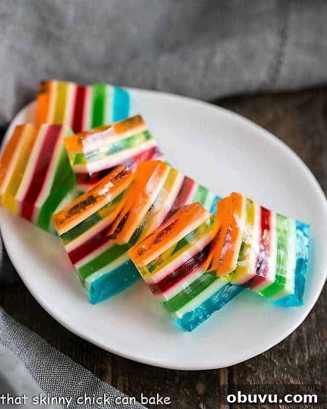 Vibrant Layered Jello Rainbow Salad - a special jello treat that can be made in many color combinations to celebrate any holiday or special occasion! Slices of Layered Jello Rainbow Salad on a white oval dish.