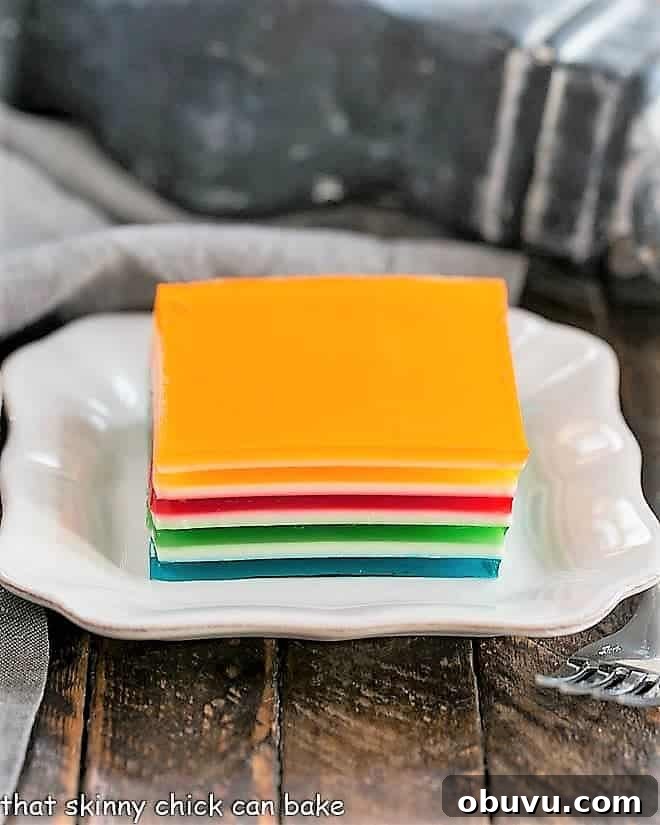 A fun vibrant Ribbon Jello Recipe is a wonderful project for kids and makes a special treat for any meal or holiday! A square of Jello Rainbow Ribbon Salad on a square white plate.