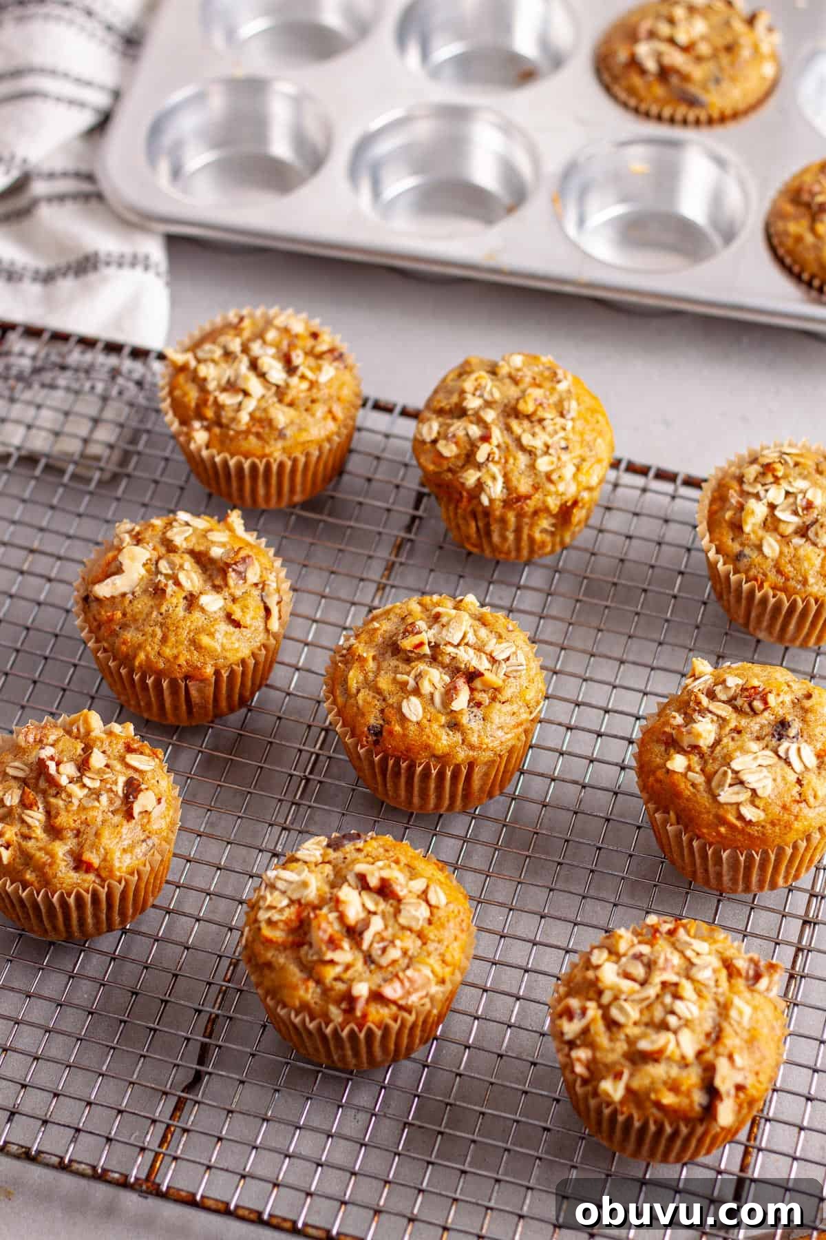 A wire rack with carrot and banana muffins cooling and a muffin tin in the background.