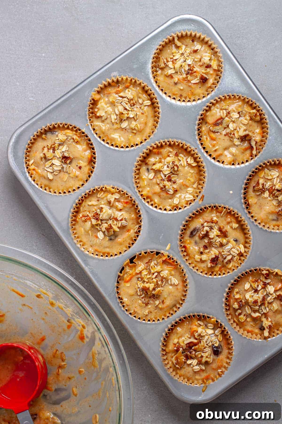Banana and carrot muffin batter in a muffin tin topped with oats and walnuts.