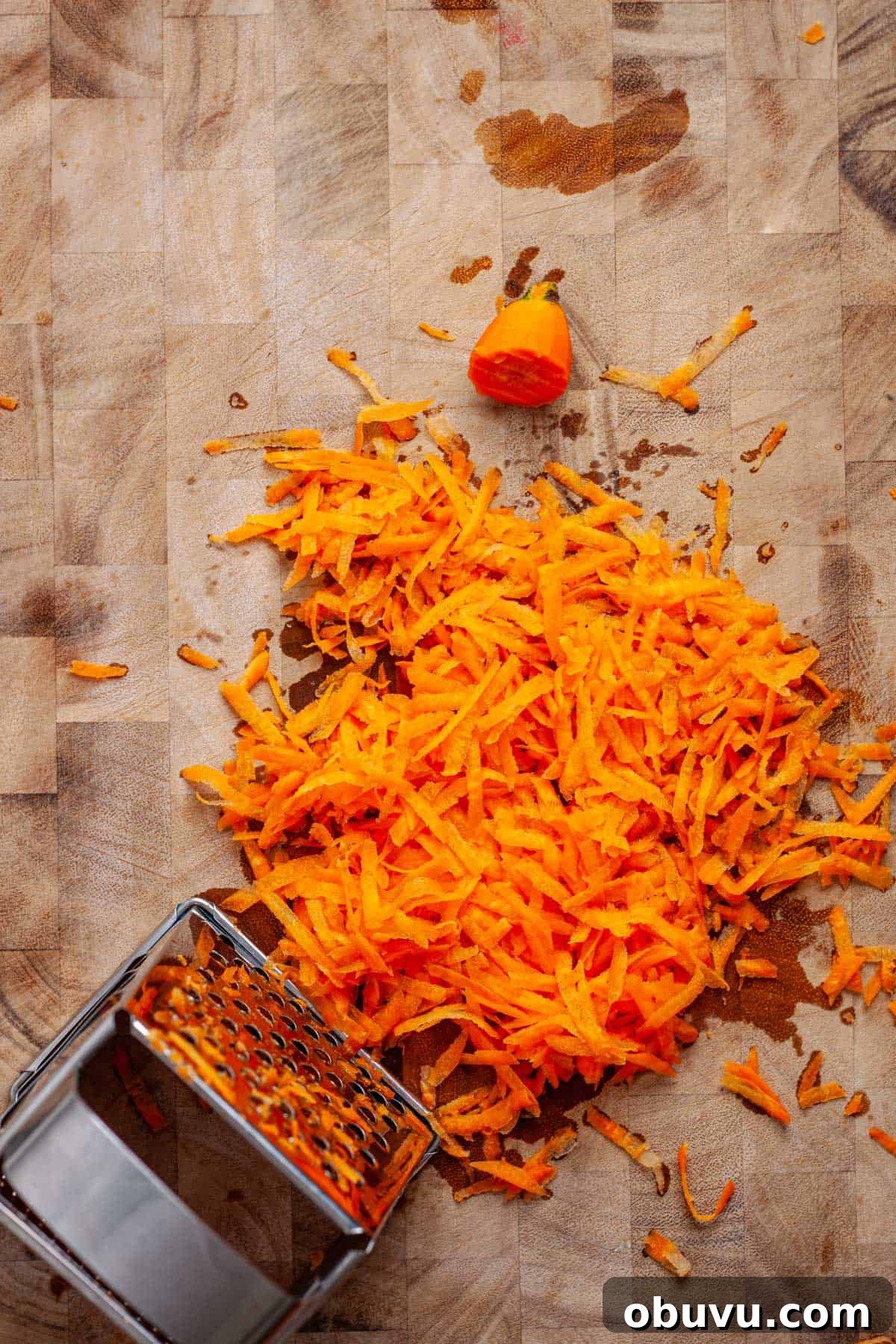 Grated carrots with a box grater on a butcherblock cutting board.