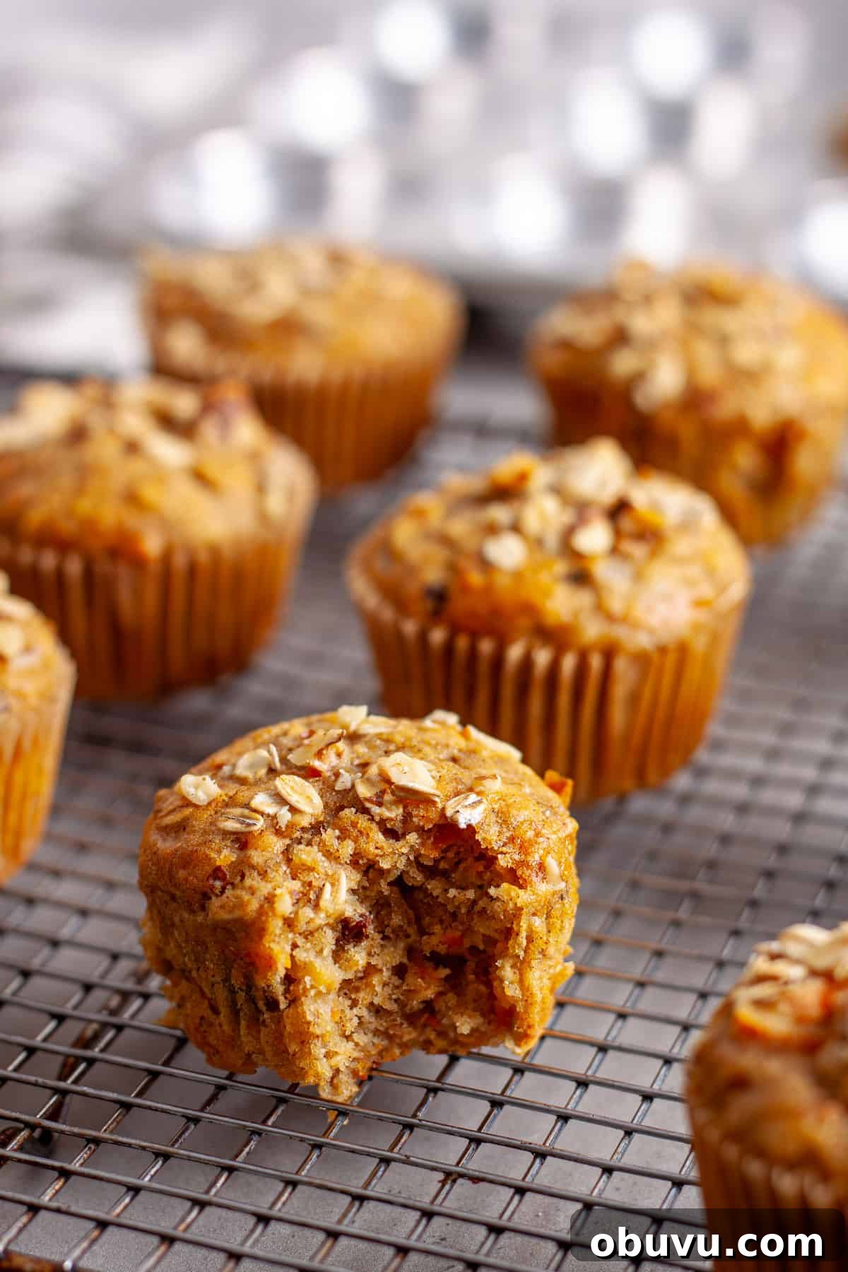 A bite taken out of a carrot banana muffin cooling on a wire rack.