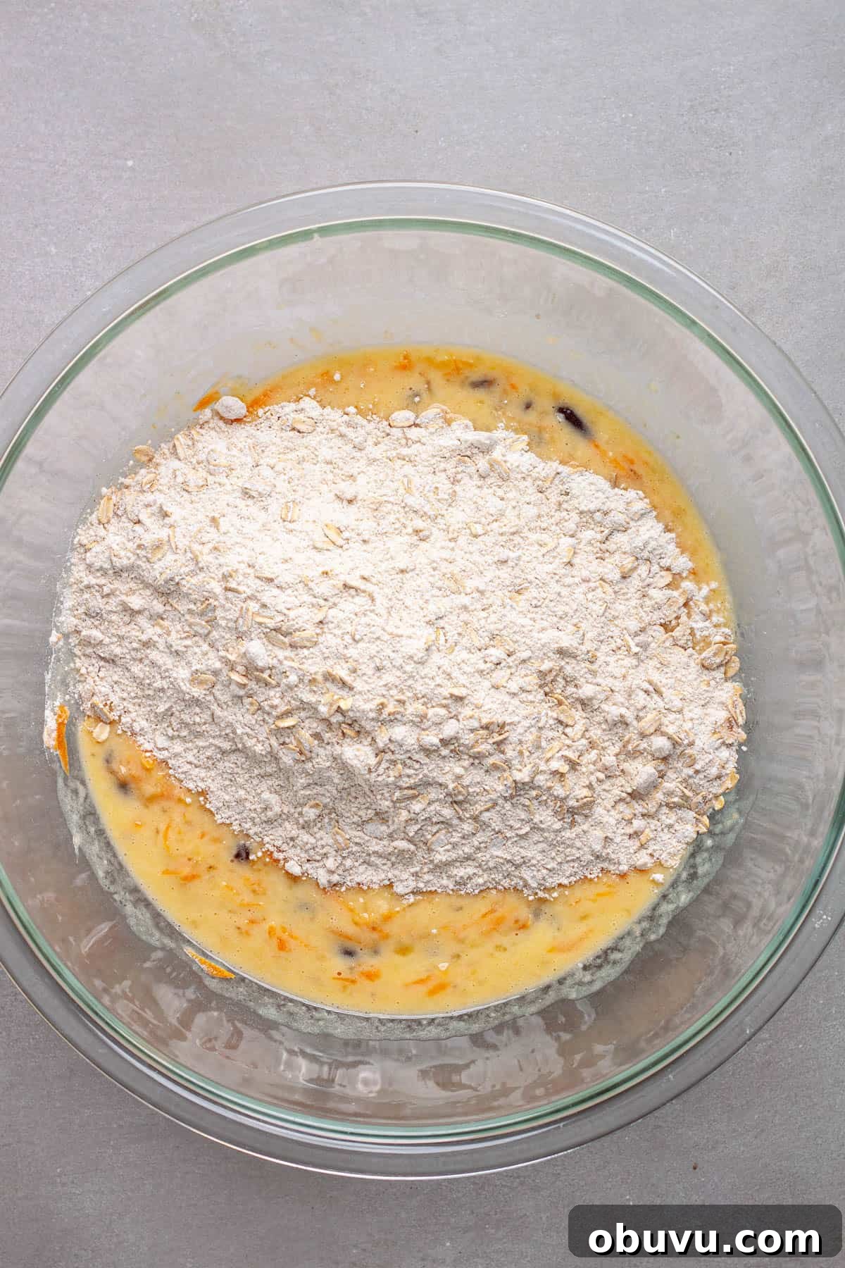 Dry ingredients for muffins added to a mixing bowl with the wet ingredients, including bananas and carrots.