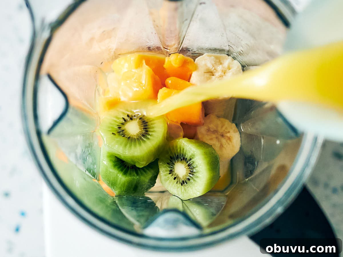 Refreshing Mango and Kiwi Smoothie Recipe for Glowing Mornings 6 Orange juice being poured into a blender with kiwi, mango, and banana.