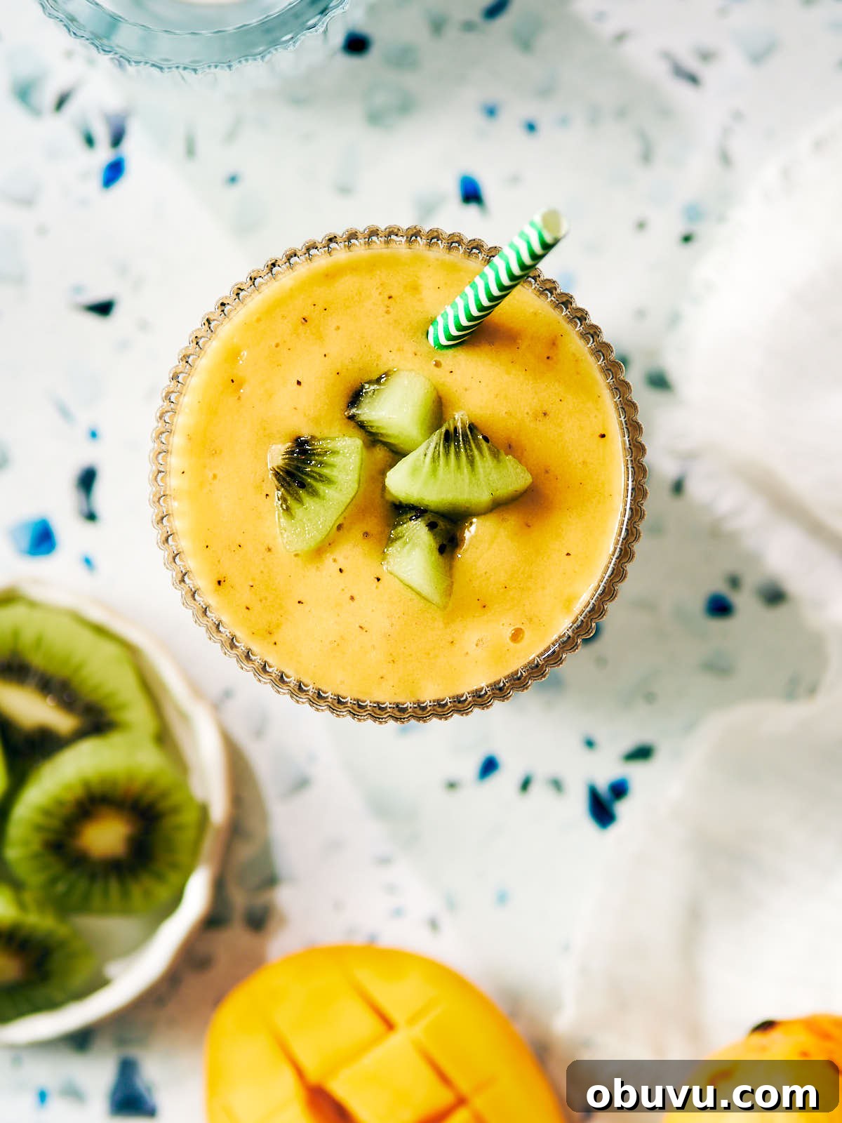 Refreshing Mango and Kiwi Smoothie Recipe for Glowing Mornings 8 Vegan mango smoothie in a glass topped with kiwi and a straw.