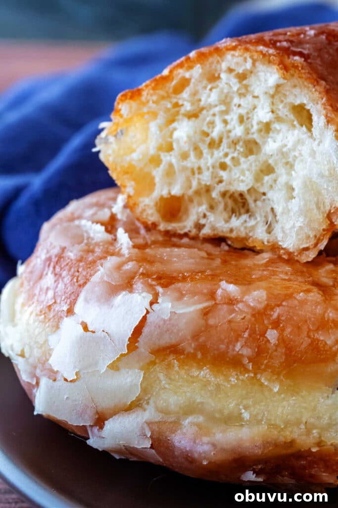 A close-up of part of two donuts stacked on top of each other showing the thin, crackly glaze and interior crumb.