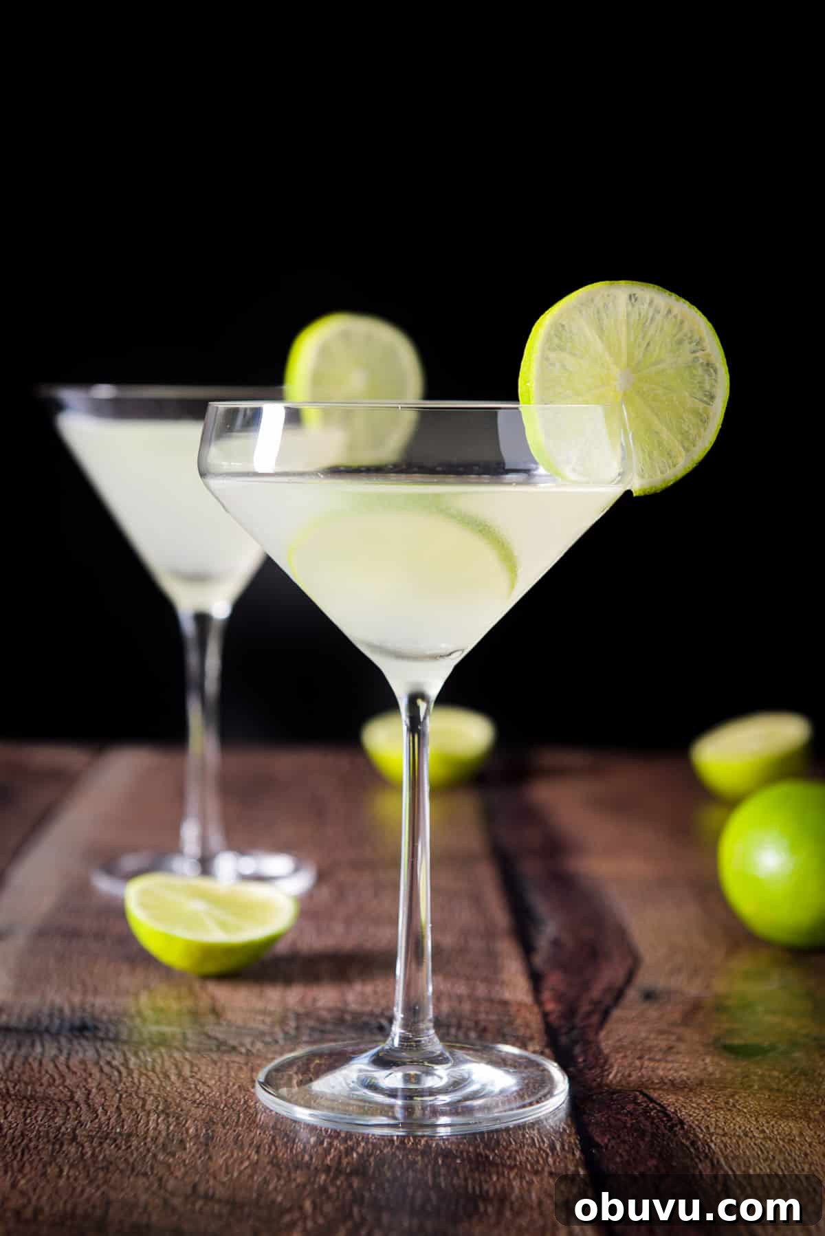Classic Kamikaze Cocktail Recipe and Serving Tips 7 Vertical view two glasses filled with the kamikaze, with limes on the table and lime wheels on the side of the glasses