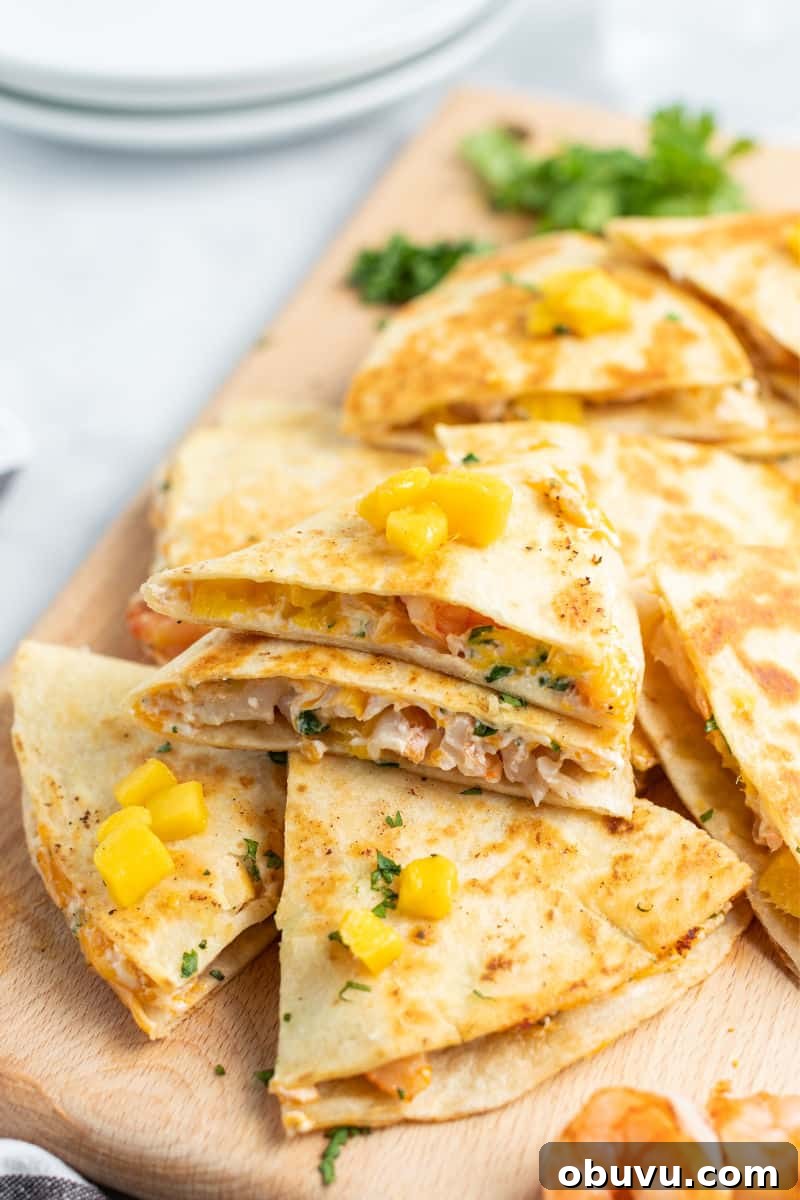 Mango & Shrimp Quesadillas are crazy good and fly off the plate! Make them with or without cilantro for a dinner win the whole family will love! shrimp quesadillas cut into slices and piled up on a cutting board