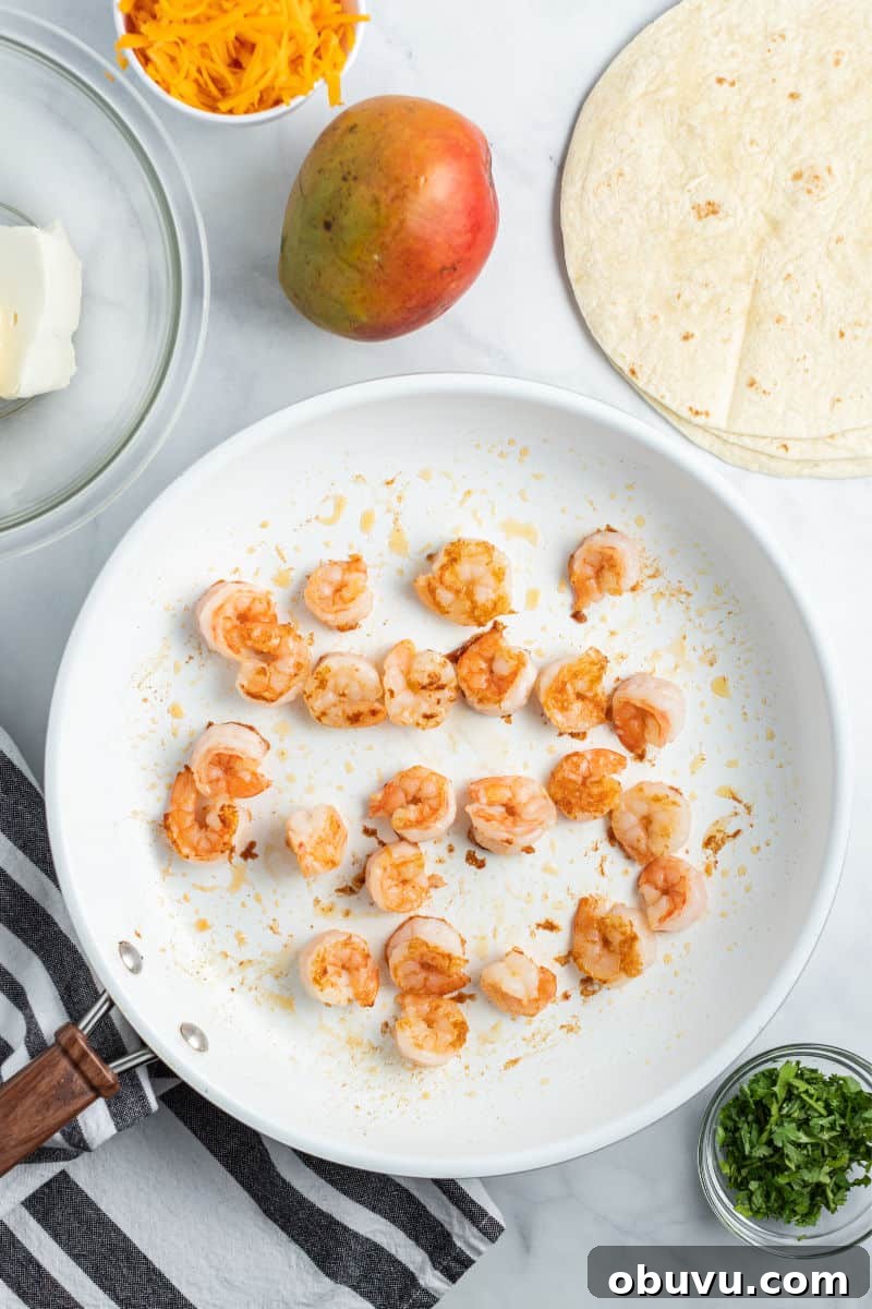 Mango & Shrimp Quesadillas are crazy good and fly off the plate! Make them with or without cilantro for a dinner win the whole family will love! ingredients to make mango & shrimp quesadillas with cooked shrimp in a skillet