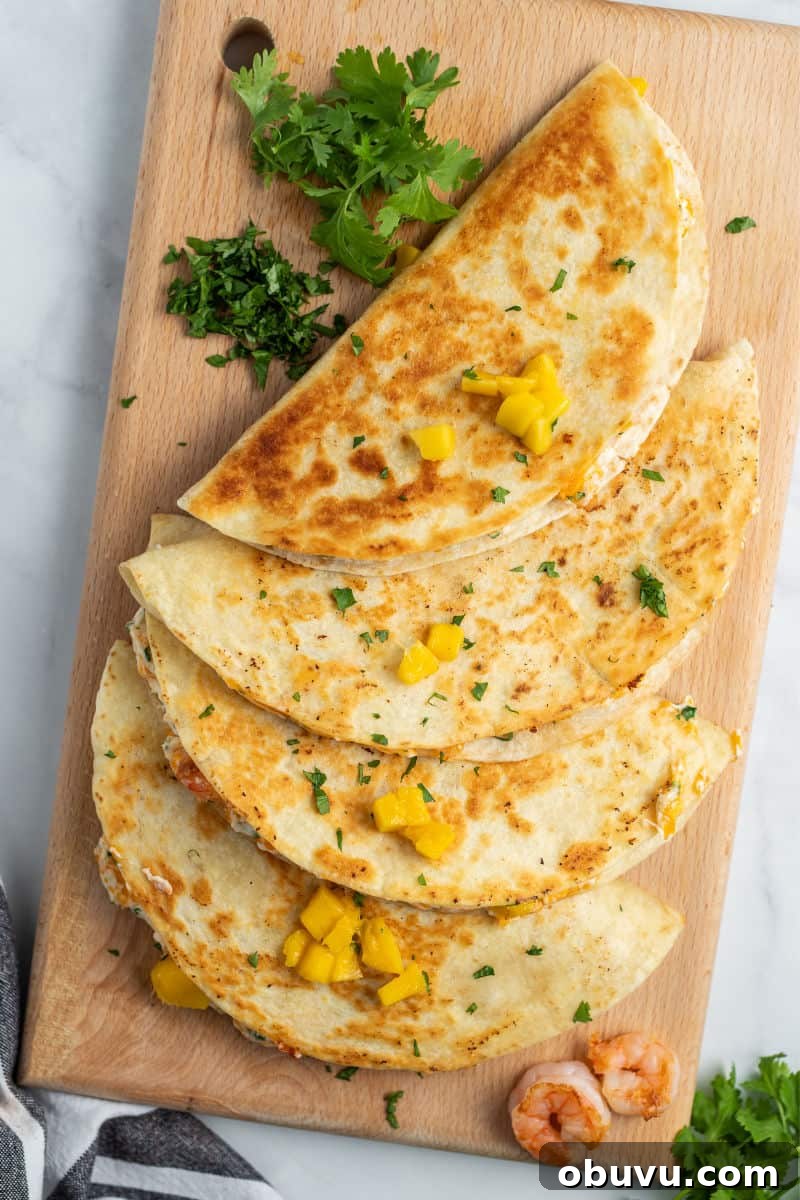 Mango & Shrimp Quesadillas are crazy good and fly off the plate! Make them with or without cilantro for a dinner win the whole family will love! four quesadillas on a cutting board with fresh cilantro