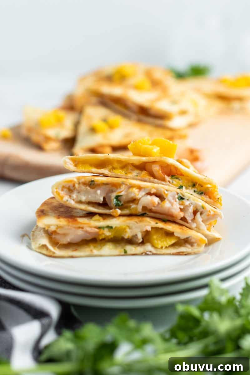 Mango & Shrimp Quesadillas are crazy good and fly off the plate! Make them with or without cilantro for a dinner win the whole family will love! slices of shrimp mango quesadilla stacked up on a small plate