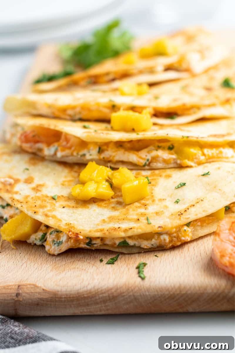 Mango & Shrimp Quesadillas are crazy good and fly off the plate! Make them with or without cilantro for a dinner win the whole family will love! side view of whole quesadillas on a cutting board to show filling