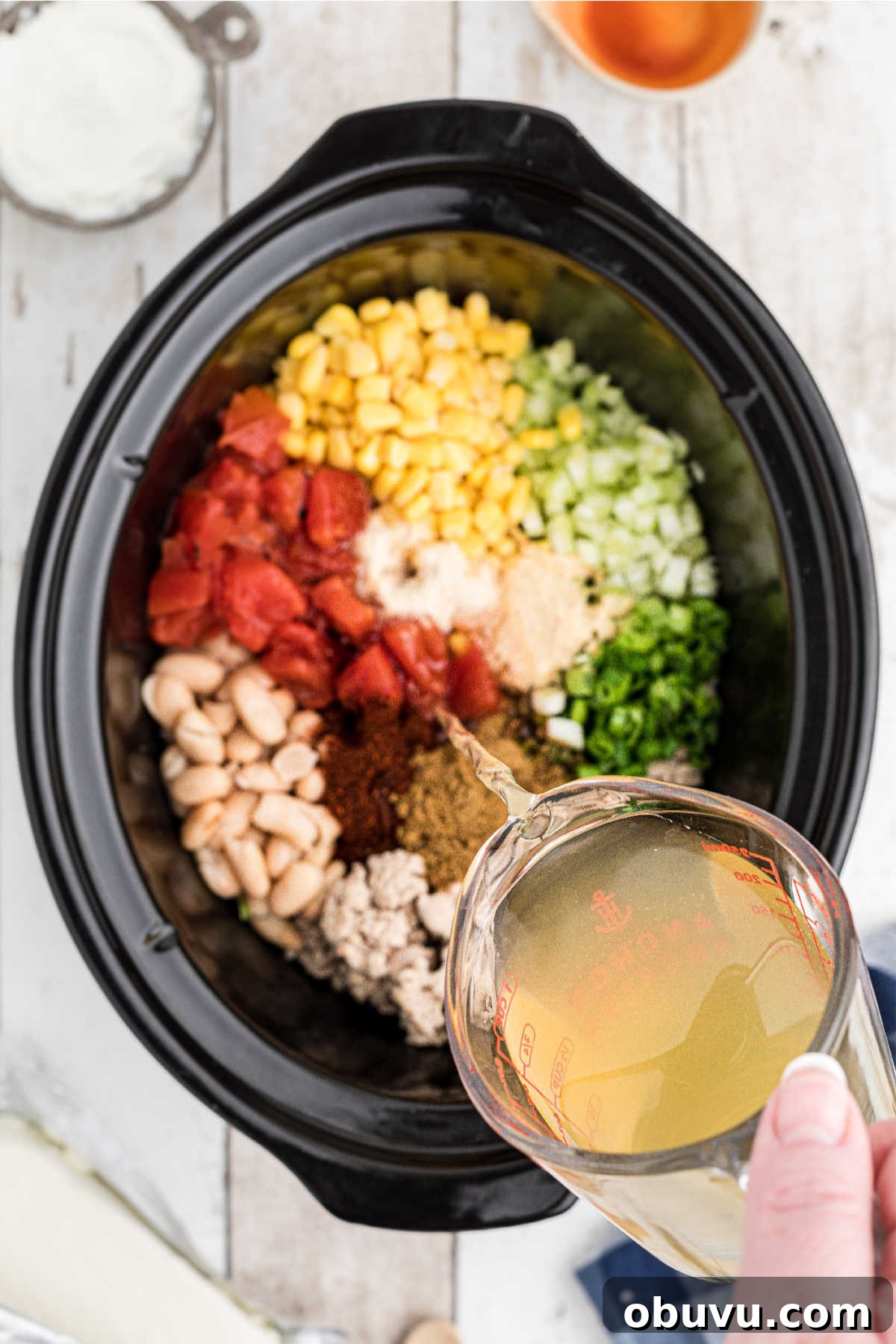 Chicken broth being poured into a crock pot full of ingredients.