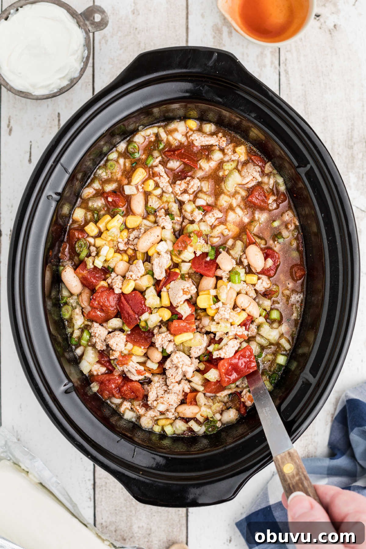 A lot of ingredients being stirred in a crock pot.