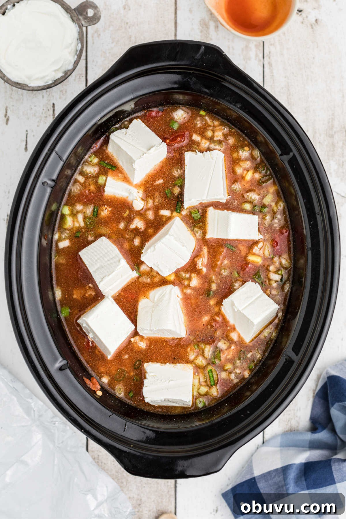 Chunks of cream cheese being added to a chili.