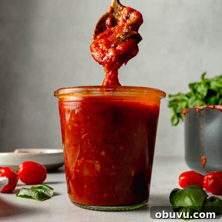 Gluten-free pizza sauce dripping from spoon into a jar filled with sauce.
