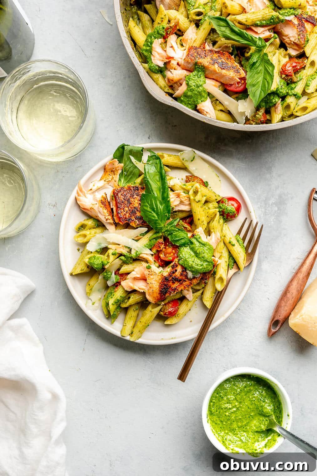 Salmon Pesto Pasta Recipe: Creamy 20-Minute Meal 11 A plate of salmon pesto pasta topped with basil leaves next to a pan of salmon pesto pasta.