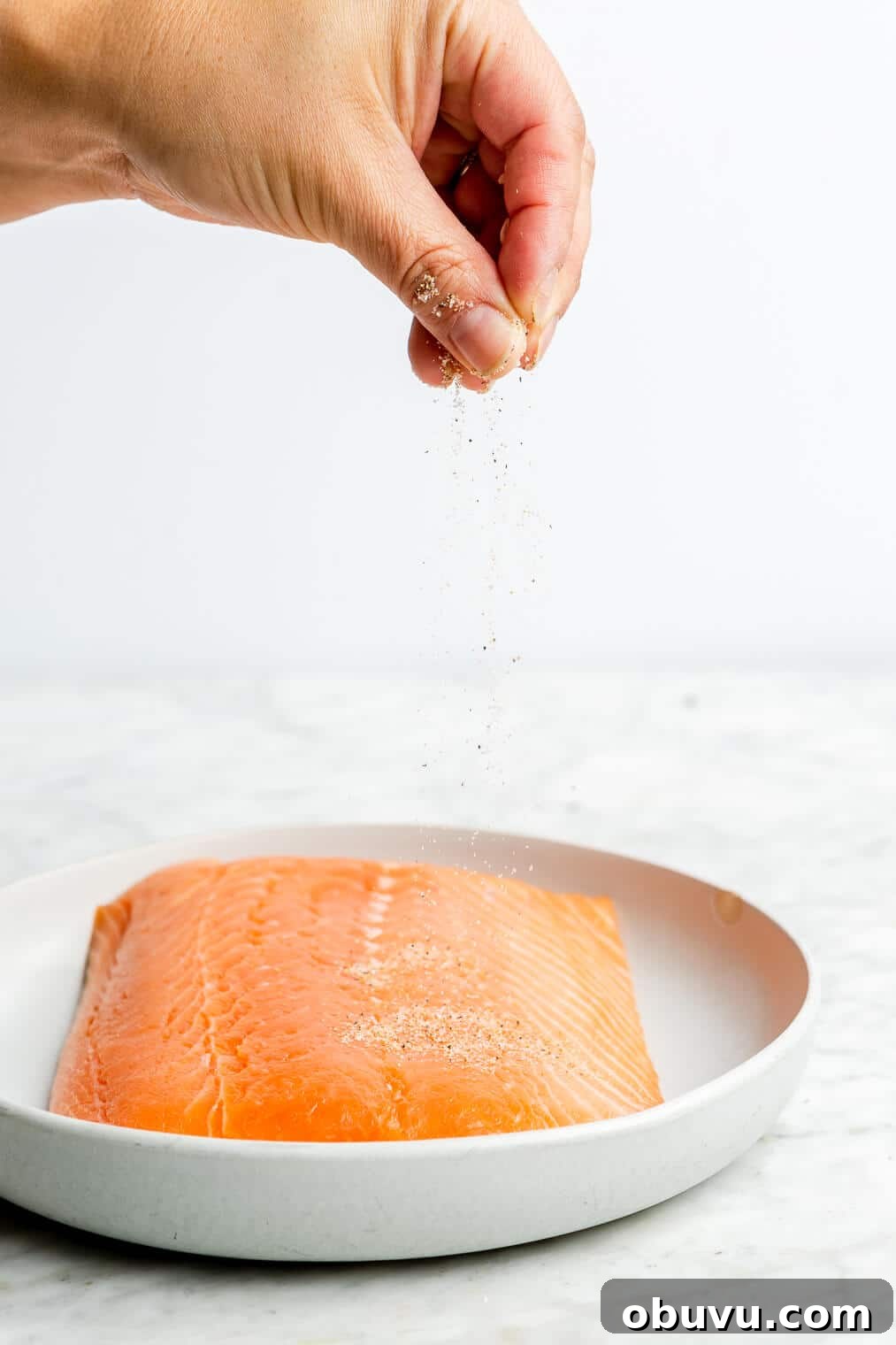 Salmon Pesto Pasta Recipe: Creamy 20-Minute Meal 4 A person sprinkling seasoning onto a filet of salmon.