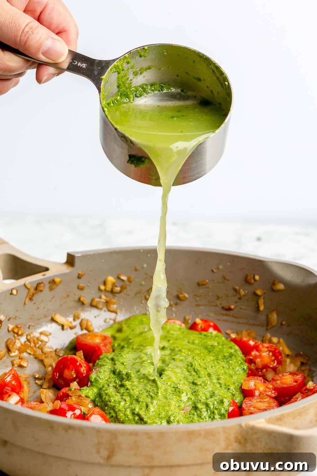 Salmon Pesto Pasta Recipe: Creamy 20-Minute Meal 8 A person adding broth to a pan of sauteed onions, cherry tomatoes, and pesto sauce.
